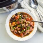 black bean sausage soup in white bowl with napkins and spoons