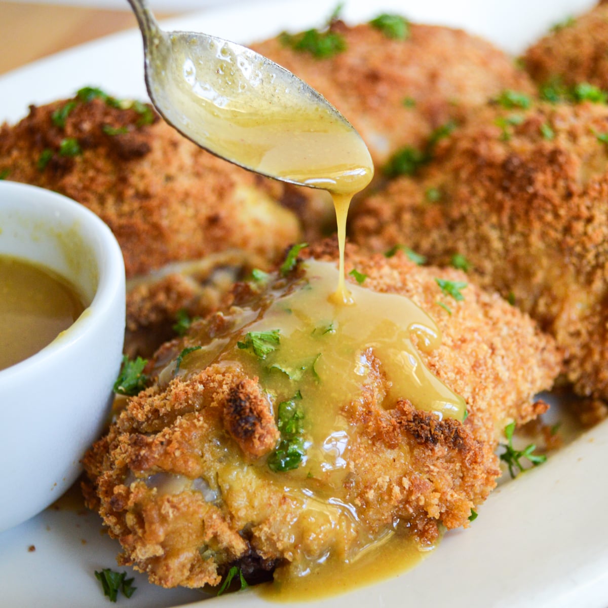 spooning maple mustard sauce on baked chicken
