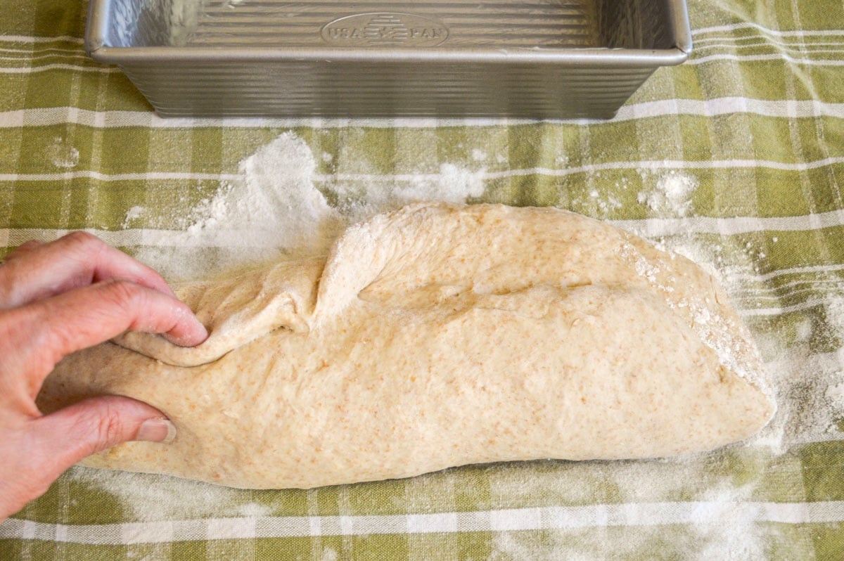 shaping bread dough into a loaf on a tea towel