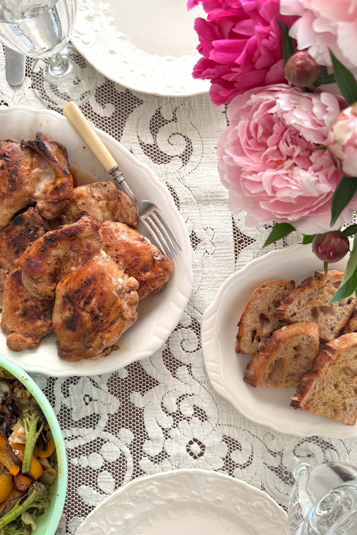 table with peonies and grilled meal on white platters