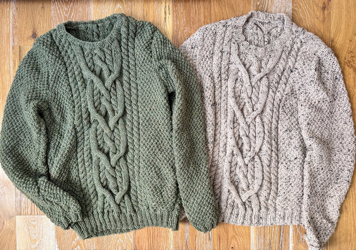 two cabled sweaters on wood floor