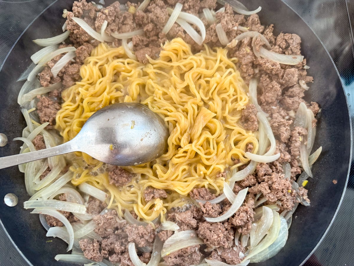 breaking up cooked noodles in pan