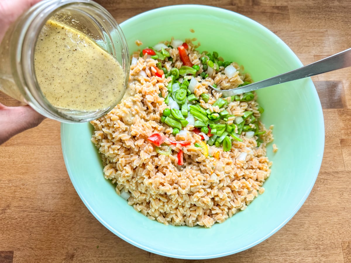 adding dressing to orzo pasta salad