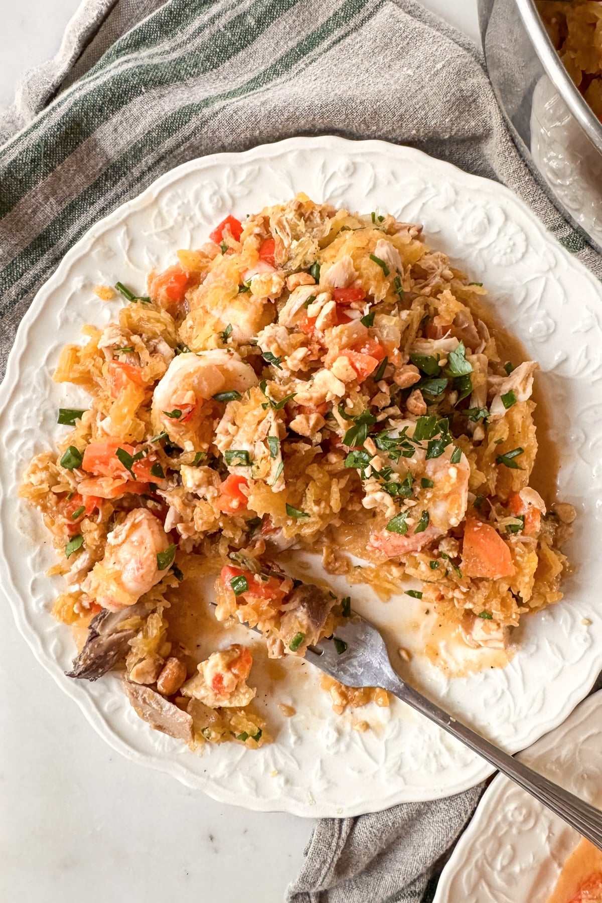 eating peanut spaghetti squash with fork from white plate